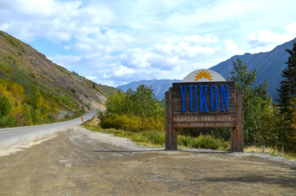 Welcome to Yukon sign on a scenic mountain road marking the entrance to Yukon Territory on a Skagway rail and bus adventure